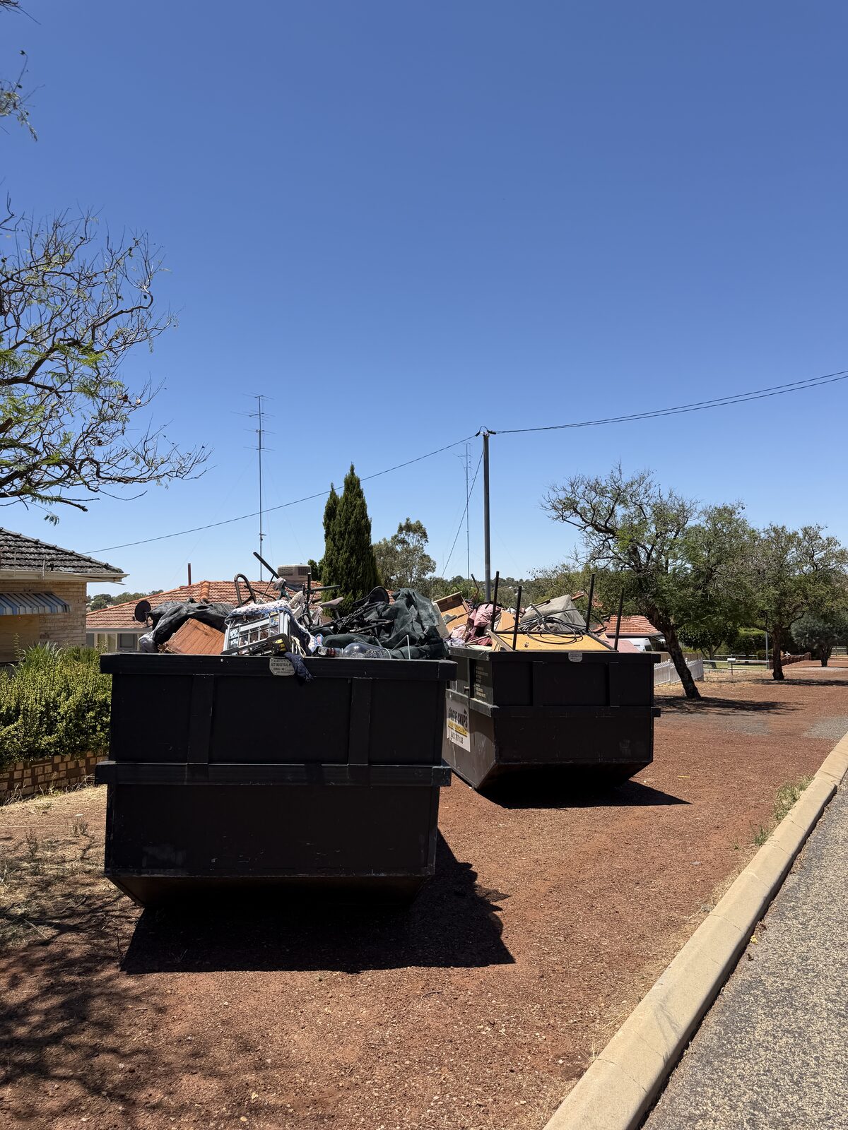 Two skip bins loaded with removed rubbish on a Perth kerb
