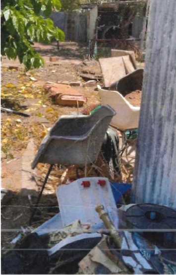 Yard cluttered with chairs, debris and overgrown areas